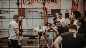 Group of athletes engaging in a competitive CrossFit workout at a gym with emphasis on strength and teamwork.